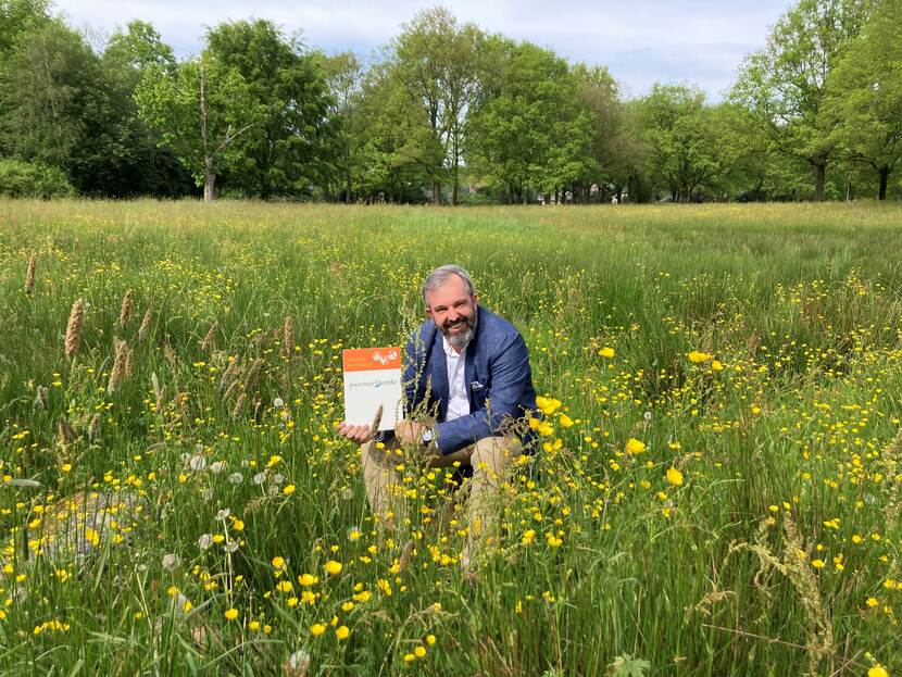Egbert van Dijk zittend in een bloeiend veld met het ondertekeningsbordje van de Nationale Bijenstrategie